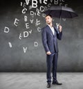 Businessman stands with umbrella under falling letters.