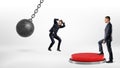 A businessman steps up on a huge floor push button to protect another man hiding from a wrecking ball.