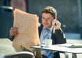 Businessman on street bar having breakfast coffee reading newspaper news talking on mobile phone Royalty Free Stock Photo