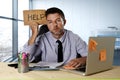 Businessman suffering stress working at computer desk holding sign asking for help looking tired exhausted