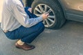 A businessman in suit crouching near his car with  punctured wheel. Man calling police using mobile phone. Street crime Royalty Free Stock Photo