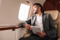 Businessman in suit holding digital tablet while looking at airplane window in private jet Royalty Free Stock Photo