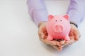 Businessman in a suit holding pink piggy bank with both hands