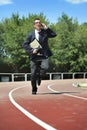 Businessman in suit and necktie carrying folder in stress on athletic track talking on mobile phone