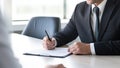 Businessman in suit signing a contract or agreement with another businessman in the background