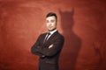 Businessman in suit standing with his arms folded, he is casting shadow of the devil on the rusty orange wall behind him