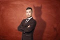 Businessman in suit standing with his arms folded, he is casting shadow of the devil on the rusty orange wall behind him Royalty Free Stock Photo