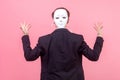 Businessman in suit standing with raised hands and back turned to camera, covering head with mask. isolated on pink background