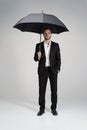 Businessman in a suit standing under black umbrella.