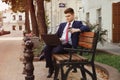 Businessman in suit surfing internet on laptop sitting on bench with take out coffee cup Royalty Free Stock Photo