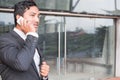 businessman in suit talking on smart phone while standing outside building. young asian male using cellphone for work at modern o Royalty Free Stock Photo