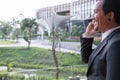 businessman in suit talking on smart phone while standing outside building. young asian male using cellphone for work at modern o Royalty Free Stock Photo