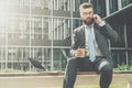 Businessman in suit and tie is sitting outside on bench,drinking coffee and talking on his cell phone.Nearby is laptop. Royalty Free Stock Photo