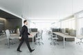 Businessman in suit walking in coworking meeting room interior with daylight, furniture and equipment. Design and ceo worker