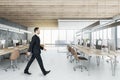 Businessman in suit walking in wooden coworking meeting room interior with daylight, furniture and equipment. Design and ceo