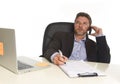 Businessman in suit working at laptop computer desk talking on mobile phone at modern office Royalty Free Stock Photo