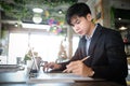 Businessman in suit working on tablet computer and writing in formation on document while sitting at modern coffee shop