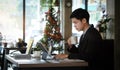 Businessman in suit working on tablet computer and writing in formation on document while sitting at modern coffee shop