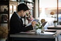 Businessman in suit working on tablet computer and writing in formation on document while sitting at modern coffee shop