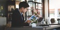 Businessman in suit working on tablet computer and writing in formation on document while sitting at modern coffee shop