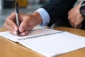 Businessman in suit writing something on notebook in office or cafe, hand of man holding pen with signature on paper report. Royalty Free Stock Photo