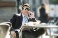 Businessman in sunglasses having breakfast coffee early morning reading newspaper news talking on mobile phone Royalty Free Stock Photo