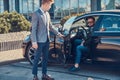 Businessman in sunglasses is talking by mobile phone while his young smart assistant is opening door for him. Royalty Free Stock Photo