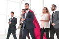 Businessman in Superman cloak and business team standing in office lobby