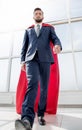 Businessman in a Superman cloak standing in a bright office