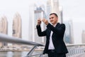 Businessman take photo mobile phone app texting outside of office in urban city with skyscrapers buildings in the background. Royalty Free Stock Photo