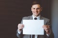 A businessman in a tie and a gray jacket holds an empty white sheet for text. Royalty Free Stock Photo