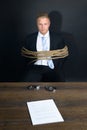 Businessman tied with rope sitting in front of table Royalty Free Stock Photo