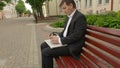 Businessman tweeting on cellphone sitting on a bench in street