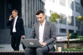 Businessman typing on laptop computer outdoor. Man in suit working with laptop while sitting on bench. Remote work Royalty Free Stock Photo