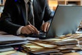 Businessman typing on laptop surrounded by documents in a modern office setting Royalty Free Stock Photo