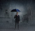 Businessman with umbrella standing over apocalyptic background. Crisis, default, setback concept.