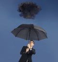 Businessman with umbrella and a black cloud with rain. Concept of crisis and financial trouble