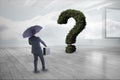 Businessman with umbrella and briefcase looking at question mark made of plants Royalty Free Stock Photo