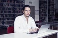 Businessman, university student wearing white shirt and eyeglasses, in a public co-working or library writing and working at lapto Royalty Free Stock Photo