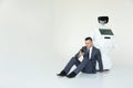Businessman uses a smartphone while sitting on the floor next to a robot. Modern Robotic Technologies. Humanoid Royalty Free Stock Photo