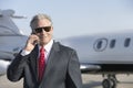 Businessman Using Cell Phone With Private Jet In Background