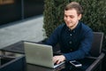 Businessman using laptop in cafe. Handsome man in dark shirn sit on the terrace. Background of green tree and blue sky Royalty Free Stock Photo