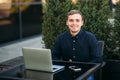 Businessman using laptop in cafe. Handsome man in dark shirn sit on the terrace. Background of green tree and blue sky Royalty Free Stock Photo