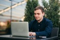 Businessman using laptop in cafe. Handsome man in dark shirn sit on the terrace. Background of green tree and blue sky Royalty Free Stock Photo