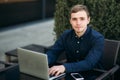 Businessman using laptop in cafe. Handsome man in dark shirn sit on the terrace. Background of green tree and blue sky Royalty Free Stock Photo