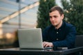 Businessman using laptop in cafe. Handsome man in dark shirn sit on the terrace. Background of green tree and blue sky Royalty Free Stock Photo