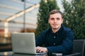 Businessman using laptop in cafe. Handsome man in dark shirn sit on the terrace. Background of green tree and blue sky Royalty Free Stock Photo