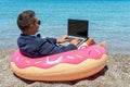 Businessman using laptop computer on inflatable donut on tropical beach. Summer vacation concept Royalty Free Stock Photo