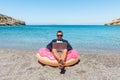 Businessman using laptop computer on inflatable donut on tropical beach. Summer vacation concept Royalty Free Stock Photo