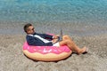 Businessman using laptop computer on inflatable donut on tropical beach. Summer vacation concept Royalty Free Stock Photo